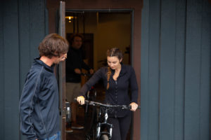 Shop attendant holding the door open for a woman wearing black as she walks her bike out