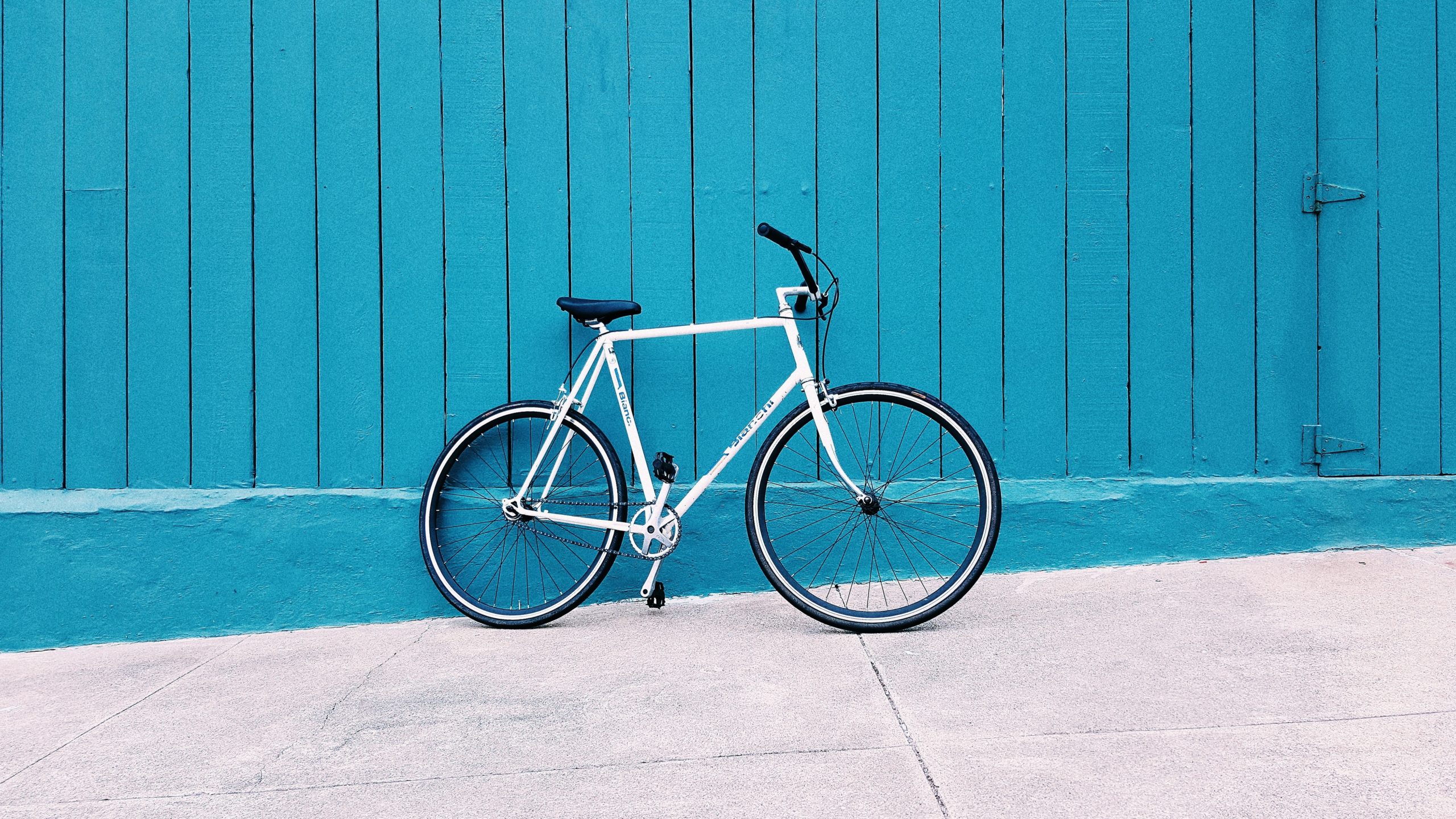 White bike leaned up against a teal wooden wall