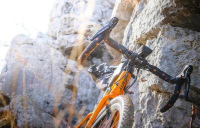 Orange gravel bike leaning up against a rock wall