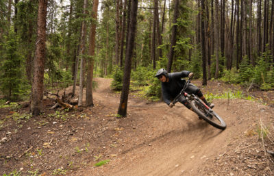 A man in all black riding a mountain bike on a dirt trail in the forest