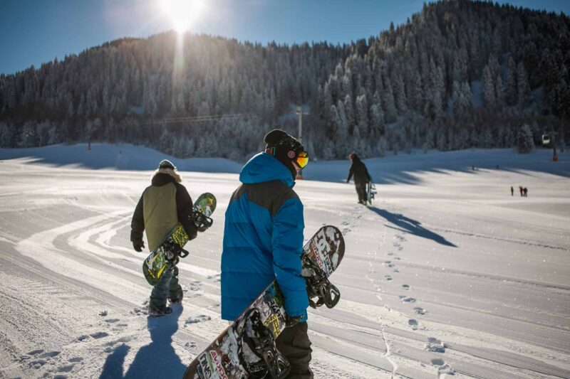 snowboarders walking on a groomed run with snow on the trees in the background